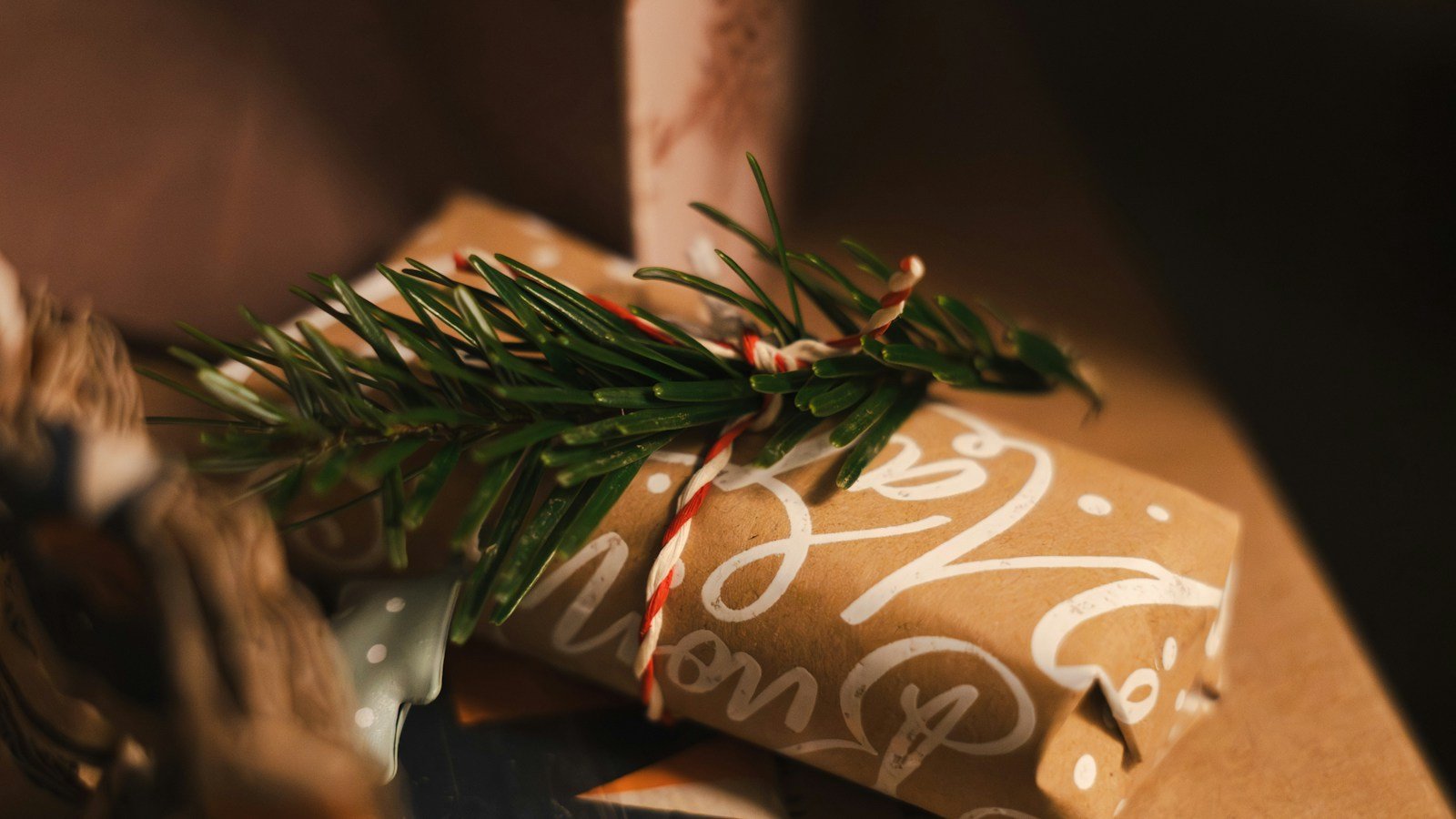 Pacchetto regalo incartato in carta marrone decorata, legato con uno spago bianco e rosso e un rametto di pino