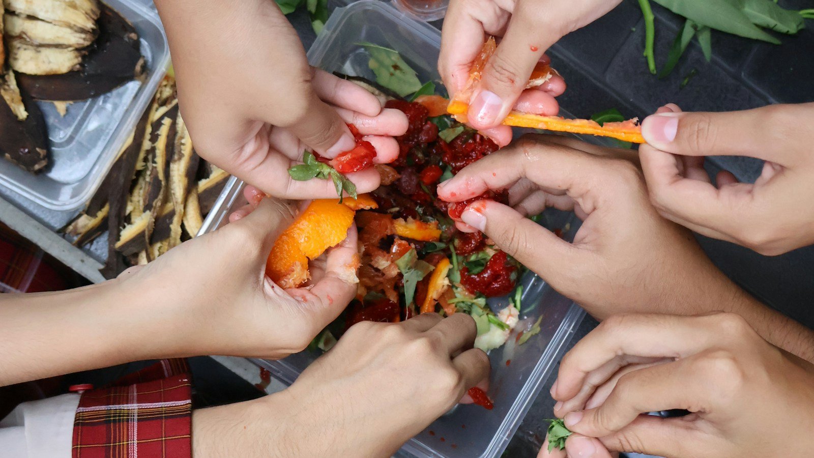 Mani di ragazzi che dividono bucce di frutta e scarti di verdura in contenitori di plastica trasparente