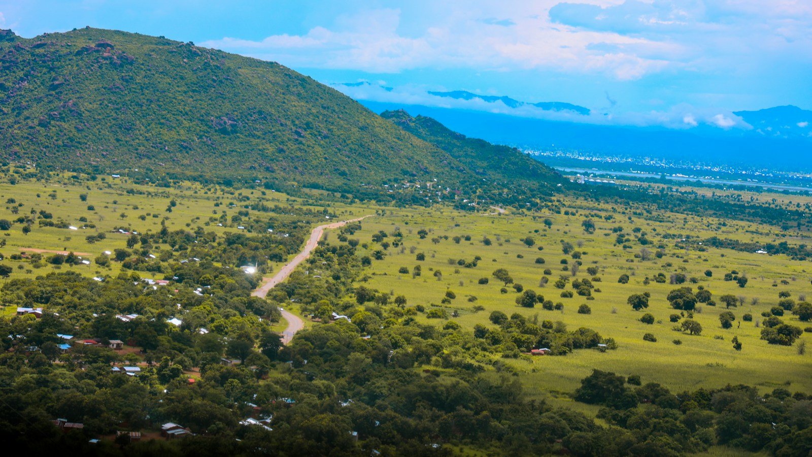 Paesaggio collinare verde vicino a Mangochi, in Malawi, con campi, alberi sparsi, case e una strada sterrata ai piedi di una montagna