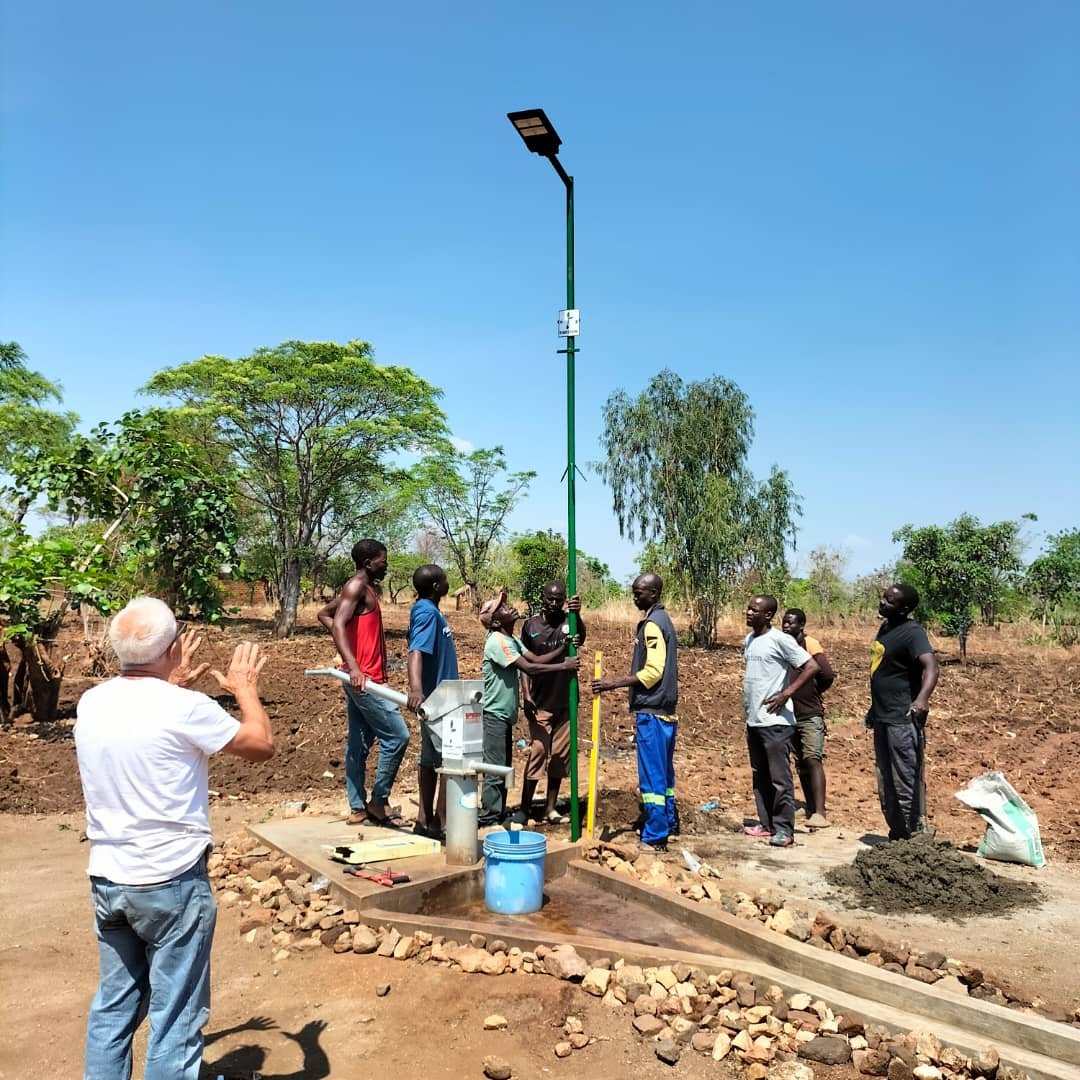 Gruppo di persone attorno a una pompa d'acqua sotto un lampione solare in Malawi