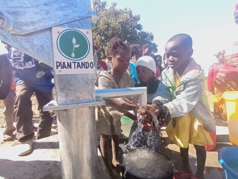Bambini alla pompa d'acqua costruita in Malawi con la targa Piantando