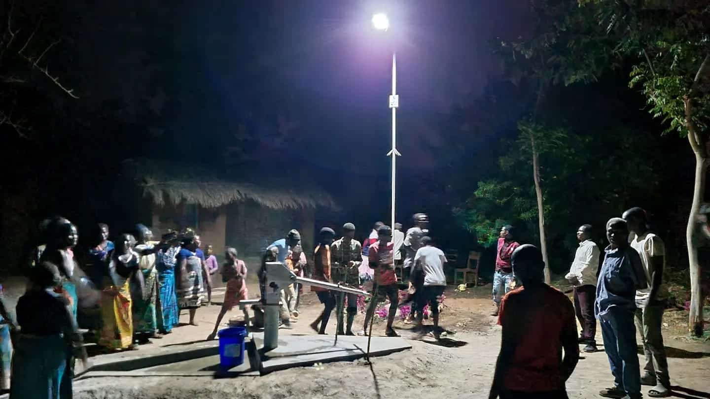 Lampione solare acceso di notte in un villaggio del Malawi con persone intorno